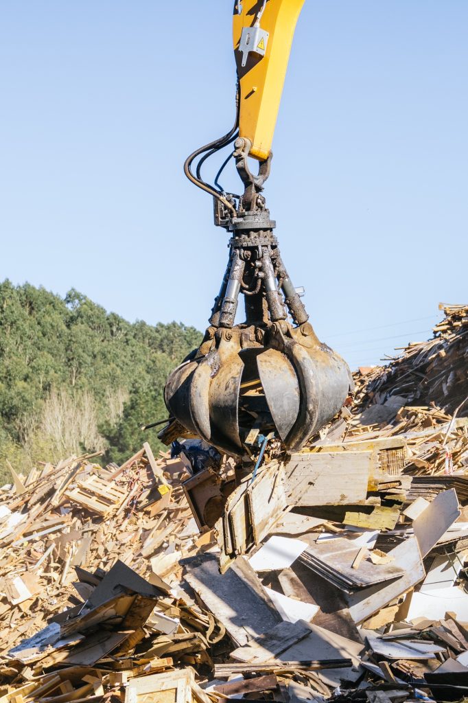 Crane handling wood waste for recycling in a sunny day